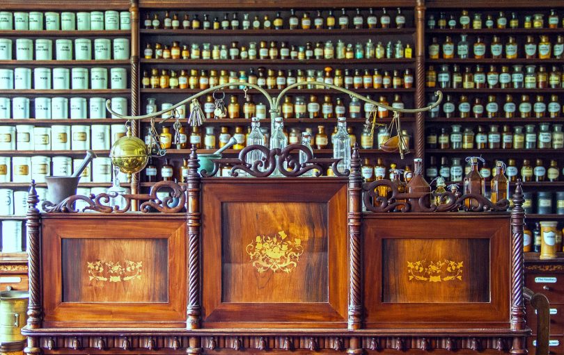 Antique apothecary shop interior with a carved wood counter and shelves of labeled medicine bottles and jars